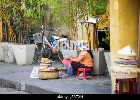 HOI AN, VIETNAM - MARZO 13: donna vietnamita di vendita di alimenti sulla strada dell antica città di Hoi An, Sito Patrimonio Mondiale dell'UNESCO il 13 marzo 2014 ad Hoi An Foto Stock