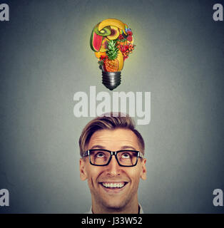 Mangiare sano idea e la dieta suggerimenti concetto. Ritratto headshot uomo cercando luce bulbo di frutti sopra la testa sul muro grigio Sfondo. Foto Stock