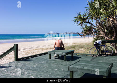 L uomo si prende una pausa dal ciclismo su un banco di lavoro con il lato di Currumbin Beach, Gold Coast, Queensland, Australia Foto Stock