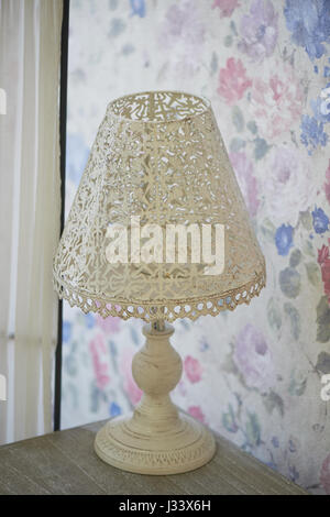 Bianco metallo traforata lampada da tavolo sorge su un comodino. Interni luminosi.shabby chic Foto Stock