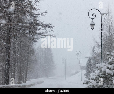 Nevica di neve che cade su di una strada in scena il francese Alpes ornato di lampada posti post Foto Stock