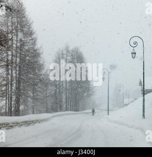 Neve caduta neve su una strada street scene in francese Alpes ornato di lampione posti e la figura di contorno a piedi silhouette Foto Stock