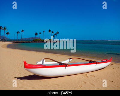 Rosso e bianco canoa outrigger su di una spiaggia di sabbia e il cielo azzurro in Hawaii Foto Stock