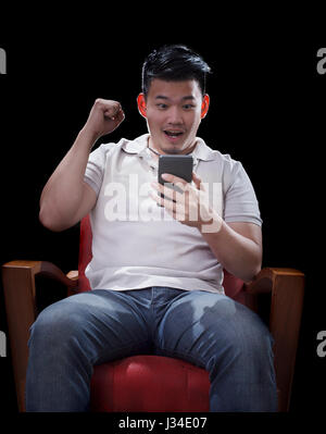 Uomo seduto su poltrone e guardare per smart phone con eccitanti faccia Foto Stock