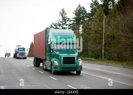 Diversi modelli di semi trucks con differenti dei rimorchi e del carico in movimento in un convoglio, uno per uno su vasta multi-lane road verso una destinazione di consegna Foto Stock