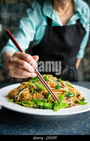 Una femmina di chef preps un noodle e neve pea stir fry con i bastoncini Foto Stock