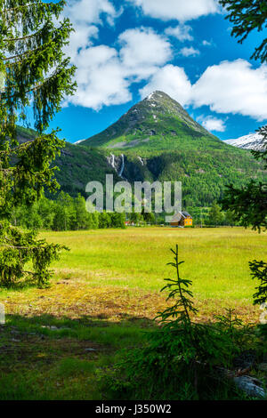 Lone a forma di cono di montagna è perfettamente incorniciato da alberi e foglie in un cielo blu sullo sfondo. Coltivatore piccolo villaggio. Foto Stock