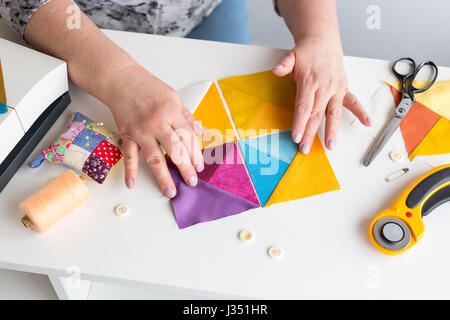 Ricamo e la trapuntatura in officina di un sarto donna su sfondo bianco - adattare al lavoro con pezzi di stoffa colorata sul tavolo con fili, tessuti, aghi della macchina per cucire coltelli rotanti. Foto Stock