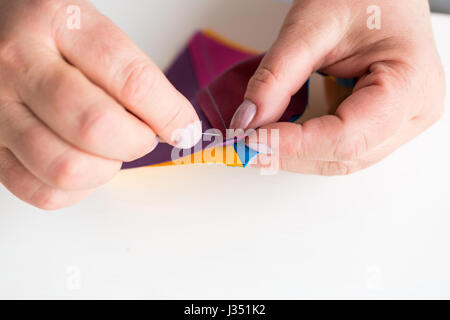 Ricamo e la trapuntatura in officina di un sarto donna su sfondo bianco - close-up sul sarto cucire a mano da parte di un ago ritagli di tessuto colorato per patchwork. Foto Stock
