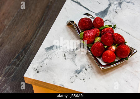 Un vaso di porcellana con fragole rosso sul bellissimo marmo bancone cucina. Foto Stock