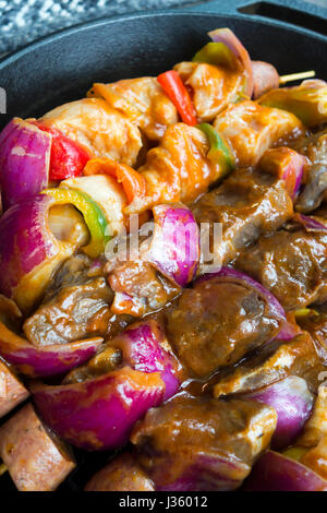 Kebab da pezzi marinato in spezie e carne in salsa filettato su spiedini con verdure tagliate a fette i peperoni e le cipolle e salsiccia impilati in padella Foto Stock