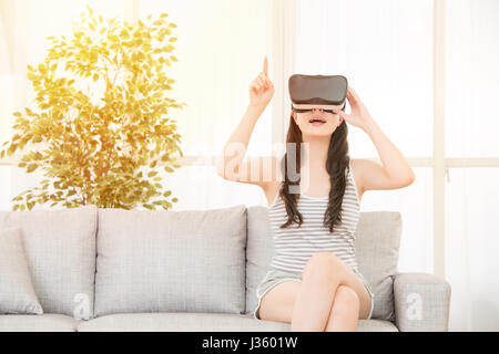 Eccitato giovane donna utilizzando un auricolare VR e touch screen su aria vivendo la realtà virtuale. razza mista asiatica modello cinese. Foto Stock