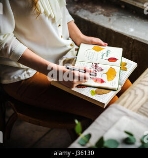 Le mani la scrittura di dettaglio di fiori secchi di raccolta in Notebook lavori fatti a mano Hobby Foto Stock