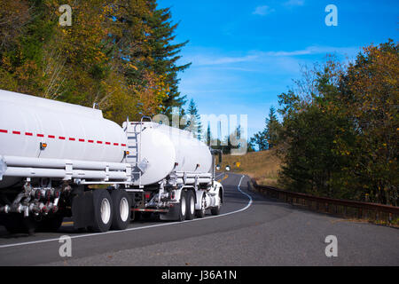 White New Big Rig semi-carrello con due rimorchi cisterna per il trasporto di carburanti e prodotti chimici si muovono attraverso l'avvolgimento di pittoresca strada d'autunno. Foto Stock