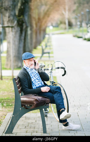 Senior l'uomo con la bicicletta e smart phone, rendendo chiamata telefonica Foto Stock