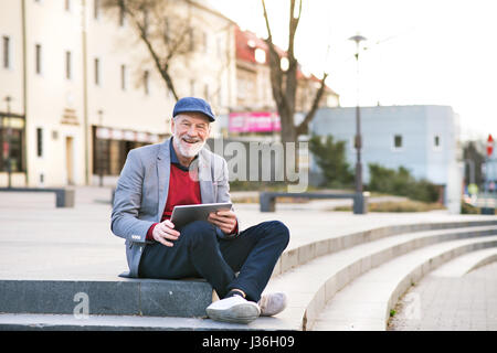 Uomo Senior in città con la compressa, rendendo chiamata telefonica Foto Stock