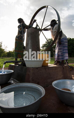 Il Burkina Faso, Gaoua , donne di recuperare acqua potabile dalla pompa acqua con ruota che gira nel villaggio / Burkina Faso Gaoua, Frauen holen Wasser von einem Brunnen mit Drehpumpe Foto Stock