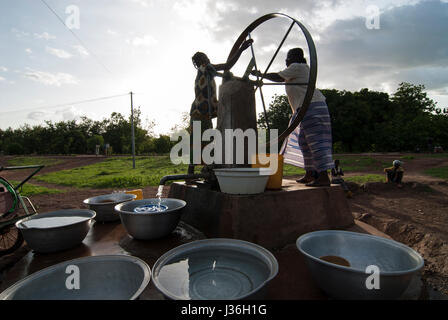 Il Burkina Faso, Gaoua , donne di recuperare acqua potabile dalla pompa acqua con ruota che gira nel villaggio / Burkina Faso Gaoua, Frauen holen Wasser von einem Brunnen mit Drehpumpe Foto Stock