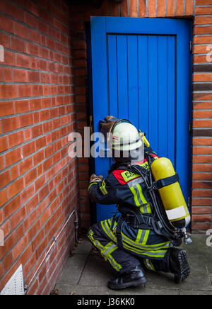 Pompiere apre una porta in azione con bottiglia di ossigeno e di protezione delle vie respiratorie maschera - HDR Foto Stock