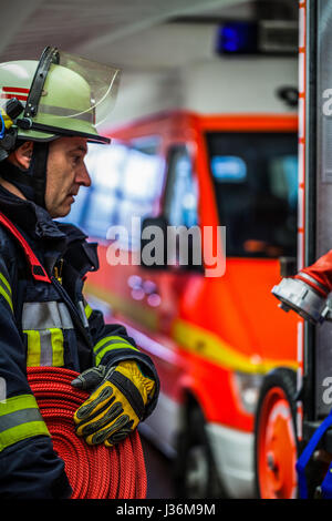 Vigile del fuoco nella stazione dei vigili del fuoco con un tubo flessibile di acqua in mano - HDR Foto Stock