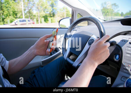 Il guidatore dietro al volante di una vettura con un telefono in mano invia un messaggio di testo durante la guida lungo la strada che potrebbe portare ad una situazione di emergenza Foto Stock