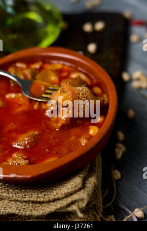 Primo piano di un vaso di terracotta con lo spagnolo callos, un tipico stufato di trippa di manzo e ceci, su una tavola in legno rustico Foto Stock