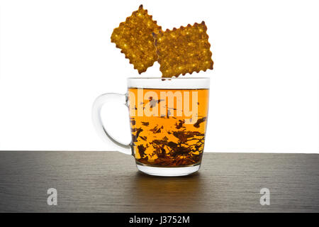 Bicchiere di vetro di tè e biscotti in caduta isolato su bianco Foto Stock