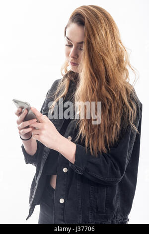 Un grazioso 15 anno vecchia ragazza texting / messaggi sullo smartphone in studio contro uno sfondo bianco nel Regno Unito Foto Stock