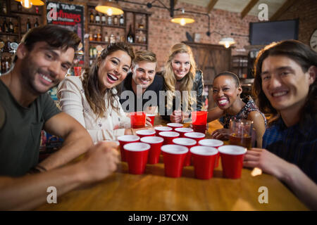 Ritratto di sorridere amici attorno a tazze usa e getta sul tavolo in bar Foto Stock