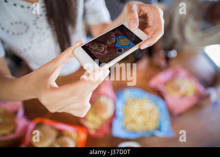 La sezione centrale della donna a fotografare il cibo attraverso mobile nel ristorante Foto Stock