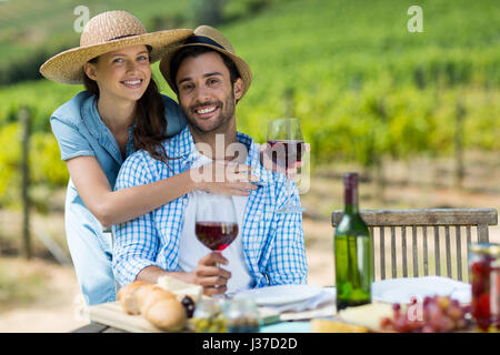 Ritratto di coppia giovane azienda vino rosso a tavola con vigneto in background Foto Stock