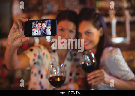 Giovani donne che prendono un selfie dal telefono cellulare mentre avente un vino rosso in pub Foto Stock