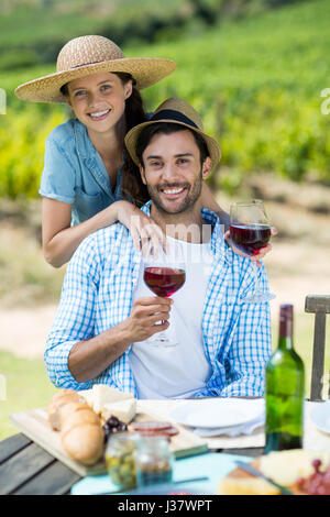 Ritratto di coppia felice tiene il vino rosso a tavola con vigneto in background Foto Stock