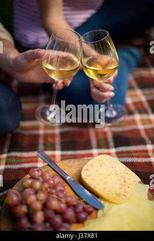 Immagine ritagliata della giovane tostare wineglasses da uva e formaggio sulla coperta picnic Foto Stock