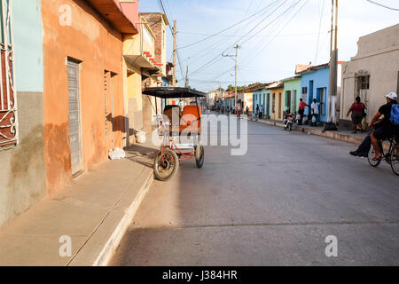 La vita di strada in Trinidad, Cuba, con una tipica cabina pedi parcheggiato sulla strada e la gente del luogo di passaggio. Foto Stock