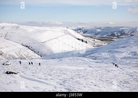 Un gruppo di escursionisti a piedi fino Kinder Scout in inverno con Edale valley in distanza. Il Peak District, REGNO UNITO Foto Stock