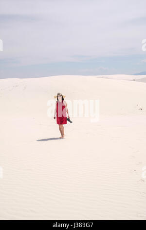 Una donna asiatica nel mantello rosso camminando sulla sommità di una duna di sabbia a White Sands National Monument, Nuovo Messico, Stati Uniti Foto Stock