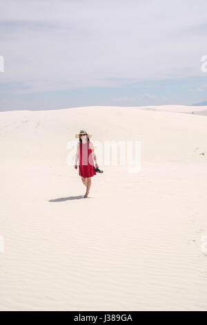 Una donna asiatica nel mantello rosso camminando sulla sommità di una duna di sabbia a White Sands National Monument, Nuovo Messico, Stati Uniti Foto Stock