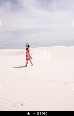 Una donna asiatica nel mantello rosso camminando sulla sommità di una duna di sabbia a White Sands National Monument, Nuovo Messico, Stati Uniti Foto Stock