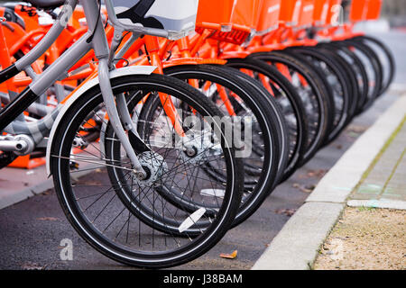 Orange bikes con cesti davanti e lucidato ruote per pagare un uso pubblico soggiorno rivestito e uno grigio bike non simbolico probabilmente altri stand out Foto Stock