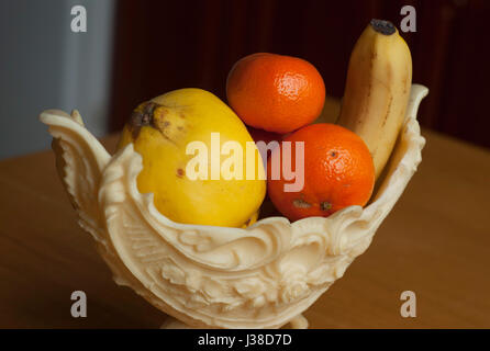Frutti in un elegante vaso in plastica sul tavolo di legno Foto Stock