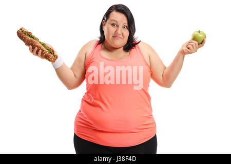 Indeciso Donna sovrappeso tenendo un panino e una mela isolati su sfondo bianco Foto Stock