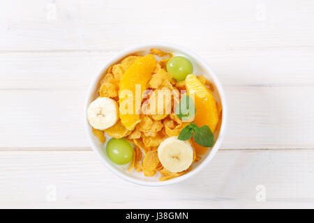 Ciotola di corn flakes con latte e frutta fresca su sfondo bianco Foto Stock