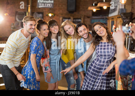 Il gruppo di amici di felice in posa mentre l uomo fotografando attraverso il telefono cellulare in pub Foto Stock