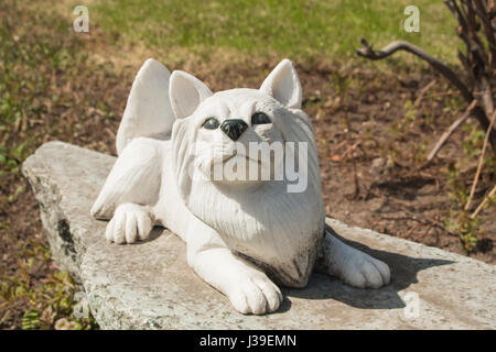 Un cane di piccola taglia marmo scultura su base in granito nel giardino di primavera. Foto Stock