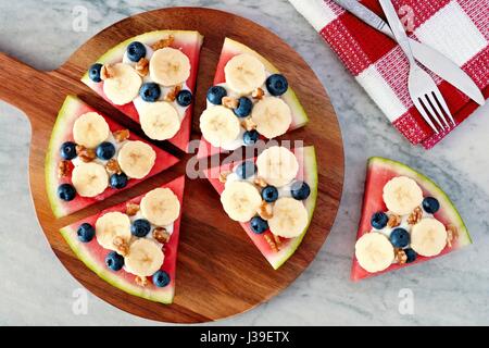 Anguria a fette di pizza con le banane, mirtilli, dadi e yogurt, sopra vista sulla scheda servente Foto Stock