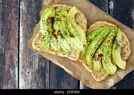 Aprire panini avocado con grano intero pane sulla carta contro un rustico sfondo di legno Foto Stock