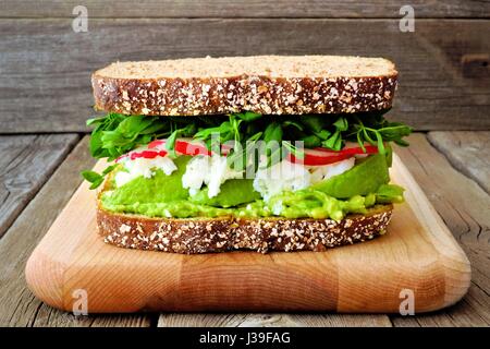 Super sandwich con avocado, albumi, ravanello e il segnale di PEA germogli su tutto il pane di grano contro un rustico sfondo legno Foto Stock