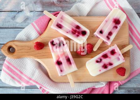 In casa lampone gelato alla vaniglia viene visualizzata su un dispositivo di compressione scheda con asciugamani su un rustico sfondo legno Foto Stock