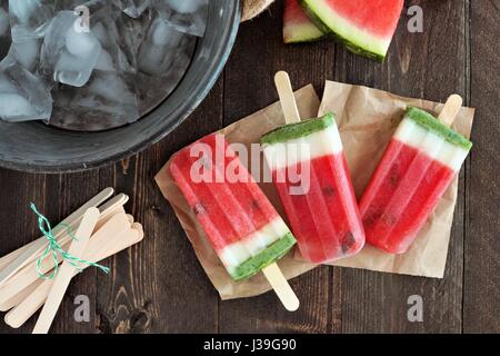 In casa di anguria popsicles su carta con il secchiello per il ghiaccio e legno rustico sfondo Foto Stock